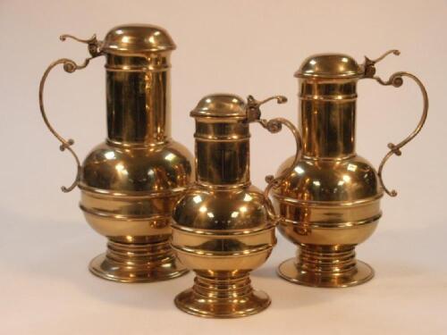 Three graduated brass flagons with scroll handles