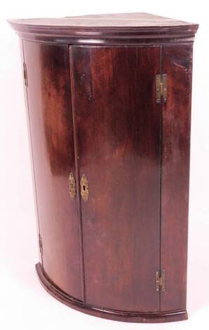 An early 19thC mahogany bow fronted corner cupboard, the over hanging top raised above two doors, on an over hanging base, 101cm H, 72cm W, 49cm D.