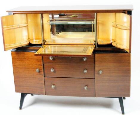 A vintage 1970s teak Beautilty cocktail cabinet, the overhanging top raised above an articulated section with concertina action shelves and three drawers beneath, flanked by cupboards on ebonised disc feet, 113cm H, 135cm W, 52cm D.