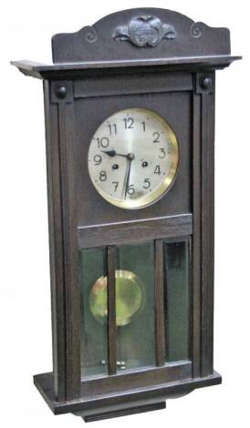 A 1920’s oak stained wall clock, the 17cm Dia. Arabic dial revealing an eight day keywind pendulum swung movement, in a carved case with glazed front, 78cm H.