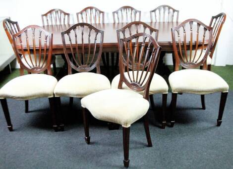 A matched 20thC dining room suite, comprising of eleven mahogany Hepplewhite style shield back dining chairs, each with overstuffed seats in straw coloured material, with serpentine fronts, on square tapering legs terminating in spade feet, 87cm H, and a 