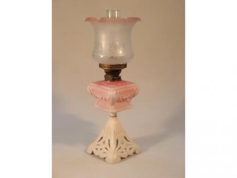 An early 20thC oil lamp with a pink moulded glass reservoir over a white metal stand