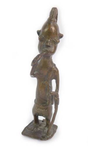 A Benin bronze figure of a tribesman, modelled standing in a lion cloth, with plaited hair, holding a staff and a pipe, 17cm H.