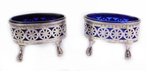 A pair of George IV silver oval salts, decorated with a band of pierced flower heads, reserve initial engraved, raised on four ball and claw feet, with blue glass liners, London 1821, 2.96oz.