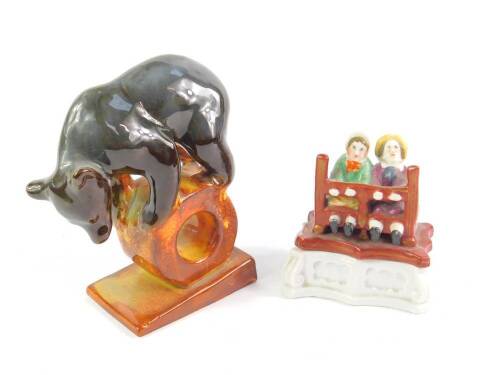 A Kona Kovo USSR porcelain figure of a circus bear on a hoop ball, 14cm H, together with a late 19thC porcelain fairing match box and cover modelled as two ladies in the stocks, 9cm W. (2)