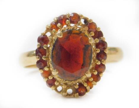 An 18ct gold garnet dress ring, with design of large central oval cut garnet, surrounded by tiny garnets (four stones missing), size N, 3.7g all in.