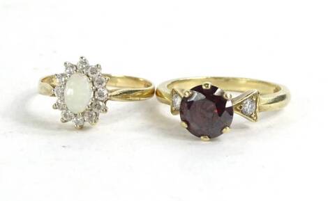 Two 9ct gold dress rings, to include a floral cluster ring with central opal, surrounded by cz stones, and another with raised central garnet, flanked by two tiny cz stones to shoulders, 5.8g all in.