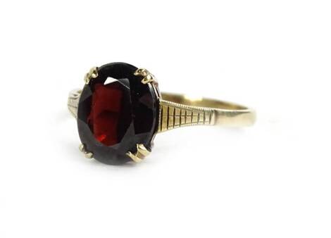 A garnet dress ring, with central oval cut garnet, in claw setting on etched design shoulders, on a plain band, yellow metal, stamped 9ct, 2.1g.