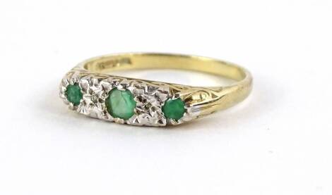 A 9ct gold emerald and diamond set dress ring, with three green emeralds and two tiny illusion set white stones, on scroll design ring head, with plain band, 2.1g all in.