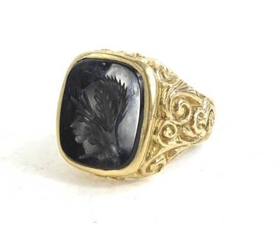 A signet ring, set with a black agate cameo, a carved warrior in profile, with c and s scroll borders and shoulders, on a later plain band, yellow metal, stamped 9ct, 12.3g.