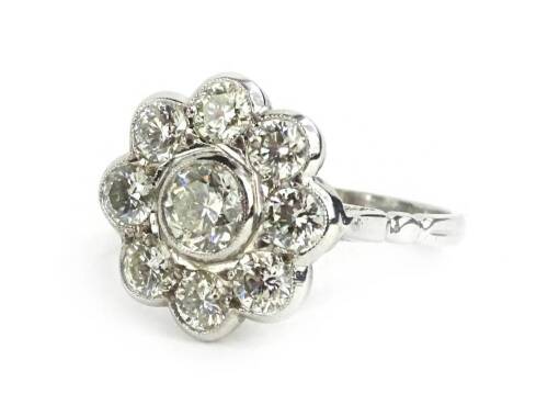 An Art Deco style diamond daisy ring, formed with round brilliant cut diamonds, in rub over setting, the central diamond approx 0.5cts, surrounded by eight smaller diamonds approx 0.2cts, on raised and pierced ring head, with etched design shoulders, on a