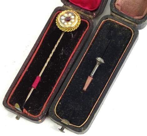 Two stickpins, to include a Victorian stick pin with large circular head, set with garnets surrounded by seed pearls, rope design borders, marked to rear 15ct, in a fitted case, and another stick pin head, set with white paste stone. (2)