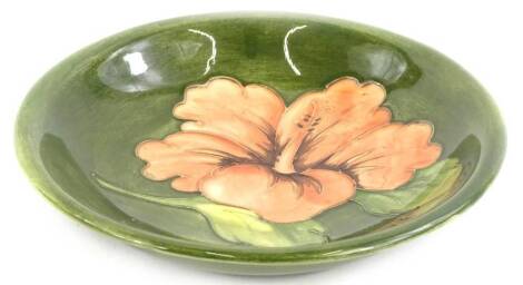 A Moorcroft pottery shallow bowl, decorated with a flower, on a green ground, impressed mark to underside and paper label, 19cm diameter.