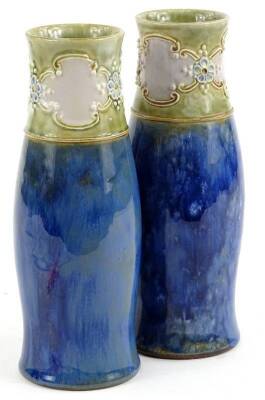 A pair of Royal Doulton stoneware vases, each decorated with a band of cartouches, flowerheads, etc., in cream on a pale green ground above a plain area of sky blue, impressed marks to underside, 20cm H.