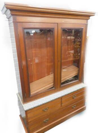 An unusual bookcase, with two glazed doors, the base with a padded top and arrangement of two short and one long drawer on a plinth, 127cm W.