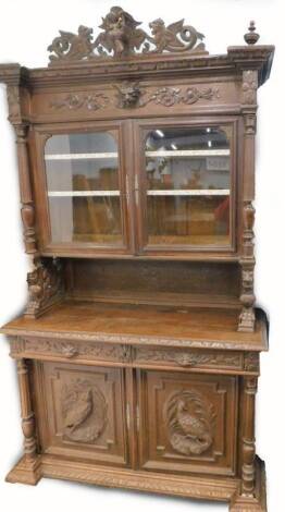 A French carved oak buffet, the top decorated with stags, beasts etc., and with two glazed doors, flanked by turned and reeded pillars, the base with two drawers above two panelled doors applied with pheasant carving on an inverted breakfront with bun fee