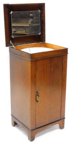 An oak wash stand cabinet, the hinged top enclosing a mirror and an enamel wash bowl with plug, etc., the door with further fitting enclosing a shelf, on bracket feet, 92cm H, 59cm diameter.