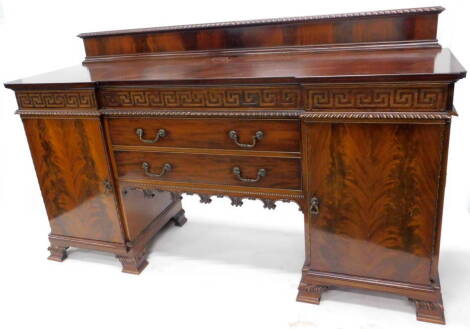 An early 20thC mahogany sideboard in George III style, with a raised back, the inverted breakfront top above a Greek key carved frieze, two drawers flanked by two doors, and a recess on ogee bracket feet, 191cm W.