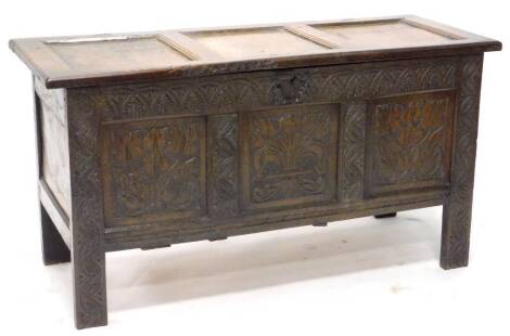 A 17thC oak coffer, with panelled hinged top, the front carved with arches, stylised tulips, leaves etc., on stiles, 127cm W.