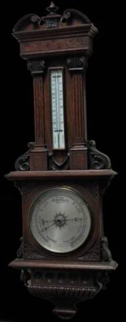 A late 19thC oak cased barometer, the 19cm Dia. silvered dial surmounted by a thermometer in a heavily carved case with broken pediment with an urn finial above carved columns, with further scroll work and a lower repeat floral patera, 100cm H.