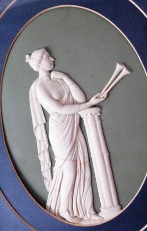 A Wedgwood Jasperware plaque, depicting a female horn player beside a column, in high relief on a green ground, 19cm x 14cm oval showing, within a modern frame.