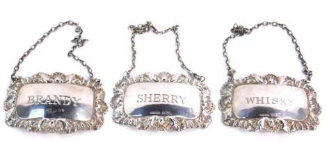 A pair of silver decanter labels for Sherry and Whisky, reserve engraved in an embossed shell and leaf scroll border, Birmingham 1995, together with a Brandy label, London 1989, 1.35oz. (3)