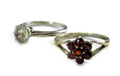 Two 9ct gold dress rings, to include a 9ct gold garnet set floral dress ring, with V shaped shoulders and a 9ct white gold dress ring, set with imitation diamond, with scroll design shoulders, 3.8g all in.