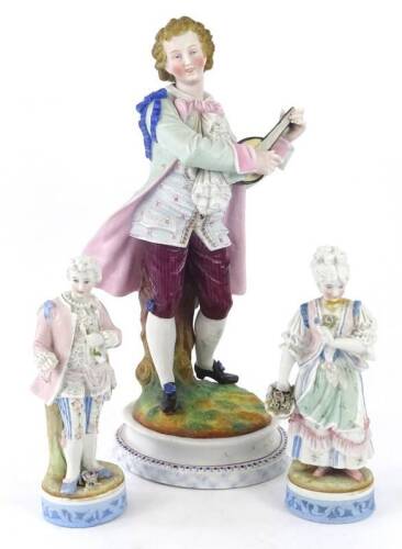 A late 19thC German bisque figure, modelled in the form of a man playing a mandolin, on a circular base, 40cm H, and two smaller similar figures. (AF)