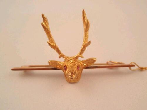 A bar brooch, stamped 9ct with attached stags head with red stone eyes, with safety chain