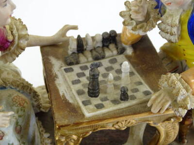 A Continental porcelain figure group, modelled on the form of people playing chess with crinoline embellishment, 32cm W, a smaller similar example of people playing backgammon, 26cm W and a Continental porcelain bell. (3) - 3