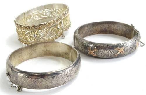 Three bangles, to include a silver bangle, with golden coloured motif birds, and c and s scroll borders, the other just with c and s scroll borders, together with a filigree bangle, possibly silver plated. (3)