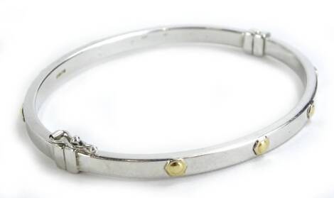 A 9ct white gold hinged bangle, with raised four circle yellow metal design, the rest on white metal banding with small hinge, boxed.