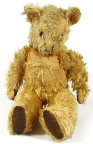 A mid 20thC English blond plush jointed teddy bear, with glass eyes, fixed mouth and articulated limbs, labelled verso, 42cm high.