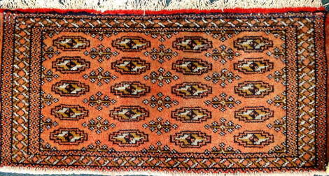 A Turkoman narrow rug or mat, with a design of medallions on a red ground with multiple borders, 105cm x 50cm.