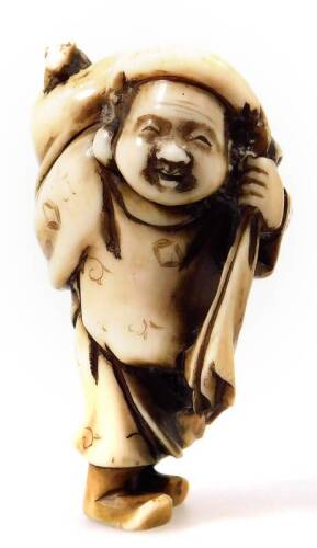 A Japanese Meiji period carved and stained ivory netsuke, formed as a man in standing pose holding sack of his shoulder, marked beneath, 6cm H.