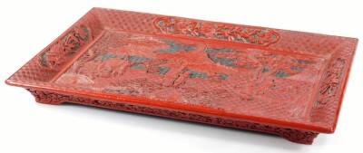 A Chinese Qing period cinnabar lacquer tray, of rectangular form, centred with a heavily carved scene of figures before mountains and trees, with an outer geometric banding broken by panels of flowers, 38cm W.