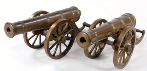 A near matching pair of polished table cannon, each with cylindrical barrels on articulated truckle bases, 26cm W. (2)