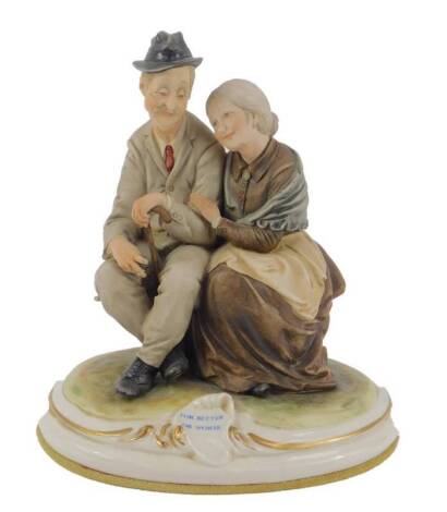 A Capo di Monte porcelain figure group 'For Better or Worse', designed by B.Merli, modelled as an elderly couple seated on a bench, on an oval rococo scroll base, 18cm H.