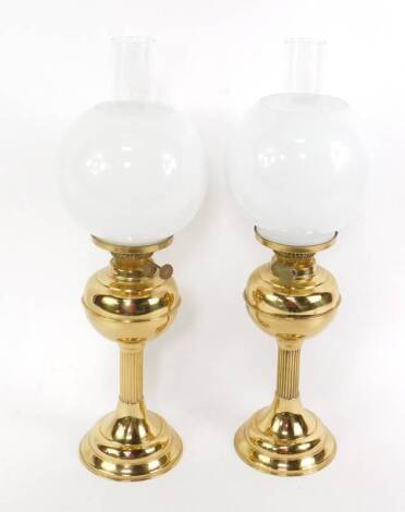 A pair of brass oil lamps, with chimneys and globular white glass shades, 58cm H.