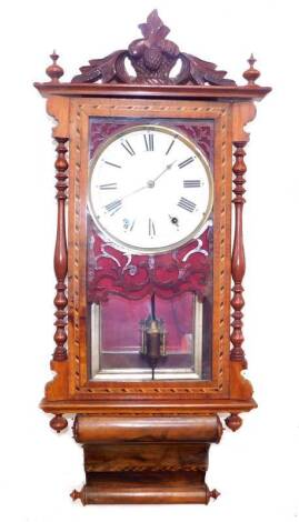 A late 19thC walnut cased wall clock, possibly American, enamel dial bearing Roman numerals, eight day movement with coil strike and mercury pendulum, the case with carved surmount, glazed door with blind fretwork, and turned columns, with key, 92cm H.