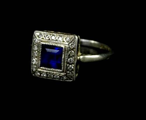 An Art Deco dress ring, with central square cut sapphire, surrounded by tiny diamonds, on a white metal band, marked 18ct plat, ring size N½, 2.2g all in.