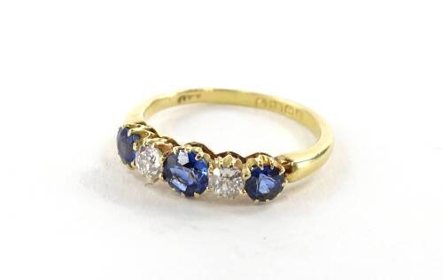 An 18ct gold sapphire and diamond five stone ring, the ring head set with three round brilliant cut sapphires, the central stone 4.2mm x 2.4mm, flanked by two smaller stones, approx 3.8mm x 2.2mm, with two round brilliant cut diamonds, 3.2mm x 2.2mm, in c