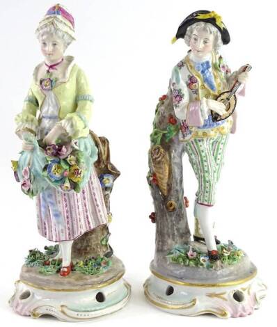 A pair of German porcelain figurines, each modelled in the form of musician and a lady carrying flowers, flower encrusted borders, rococo scroll pierced and gilt base, 29cm H.