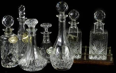 A collection of cut glass decanters and stoppers, each of differing form, to include a pair mounted in a tantalus, decanter labels etc.