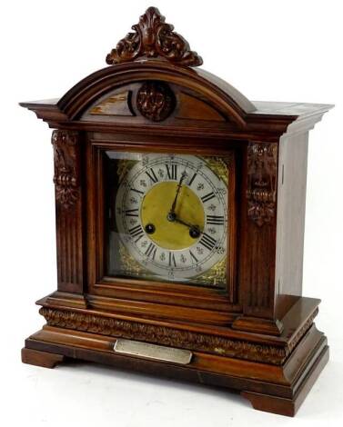 A German mantel clock, in a walnut case, the crest decorated with a lion mask above a squared dial, with silver chaptering, and gilt metal spandrels, the plinth with a silver presentation plaque, engraved Presented to H Rhodes, the remainder indistinct, 4