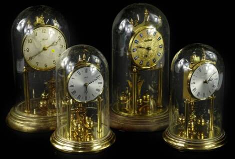 Four brass and brass effect anniversary type clocks, to include an example stamped Kundo, another Hermle, in glass domes, 30cm H, the other two clocks with Perspex domes. Provenance: This timepiece formed part of Luke Jerram's installation Harrison's Gard