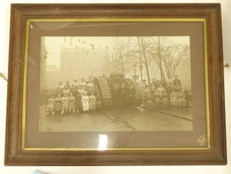 An early 20thC black and white photograph, depicting a First World War tank, various figures, female ammunition workers etc., stamped Heawood, Leicester & Melton, in an oak frame, 89cm x 51cm.