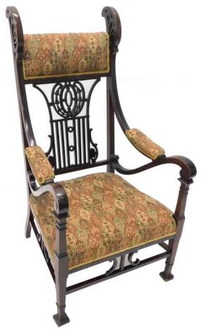 An Edwardian mahogany armchair, with a padded back, arm rests and seat, the back with pierced rails, carved with flowers, ovals etc., on square tapering legs and block feet.