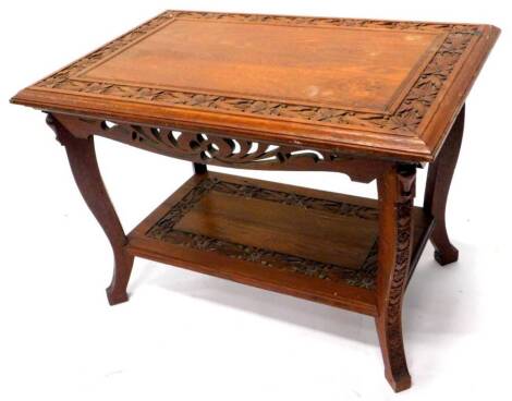 An early 20thC teak two tier table in Art Nouveau style, the rectangular top with floral carved border and a moulded edge above a pierced frieze, on shaped legs with undertier, 64cm H, the top 60cm x 91cm.