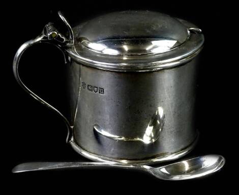 A George V cylindrical mustard pot, with domed cover and shaped thumb piece and blue glass liner and an associated mustard spoon, London 1915, weighable silver 2¼oz.